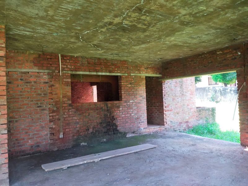 An unfinished open-plan interior space featuring exposed brick walls and a raw concrete ceiling, currently in a shell condition awaiting completion.