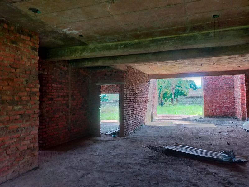 An unfinished open-plan interior space featuring exposed brick walls and concrete structural elements, currently in a shell construction state.