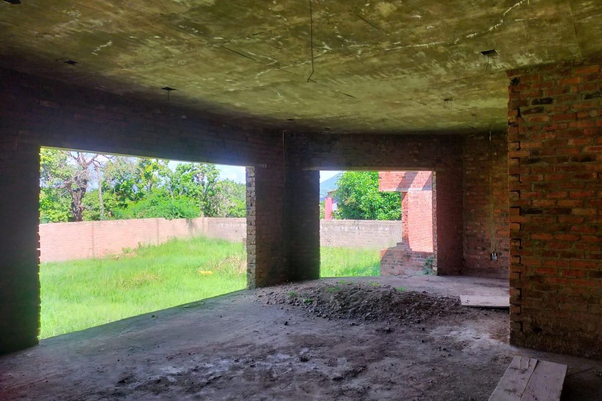 An unfinished interior space featuring exposed brick walls and concrete flooring, currently in a shell condition awaiting completion and interior finishes.