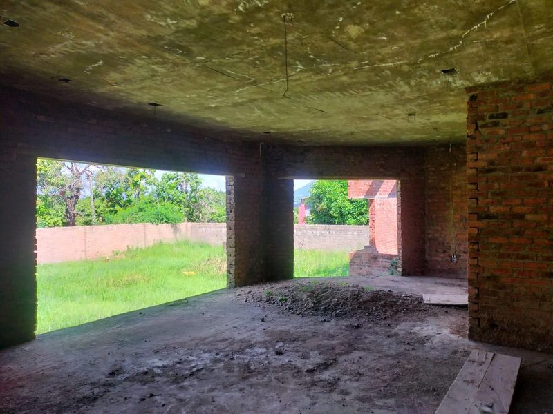 An unfinished interior space featuring exposed brick walls and concrete flooring, currently in a shell condition awaiting completion and interior finishes.