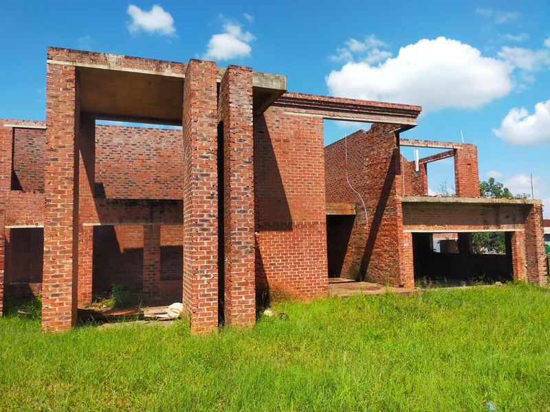 An unfinished residential property structure featuring exposed brickwork and concrete slabs, currently in the early stages of construction.