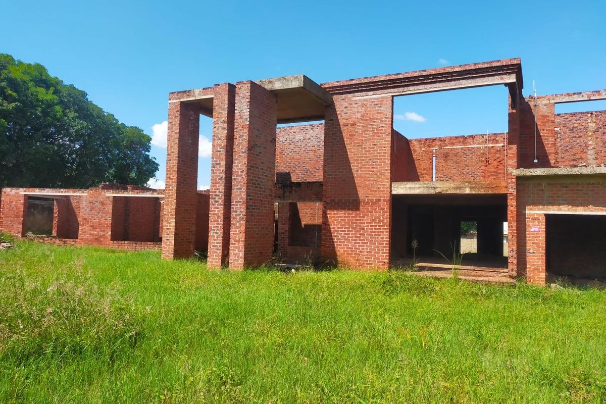 An unfinished residential structure featuring exposed brickwork and concrete framing, currently in the early stages of construction.