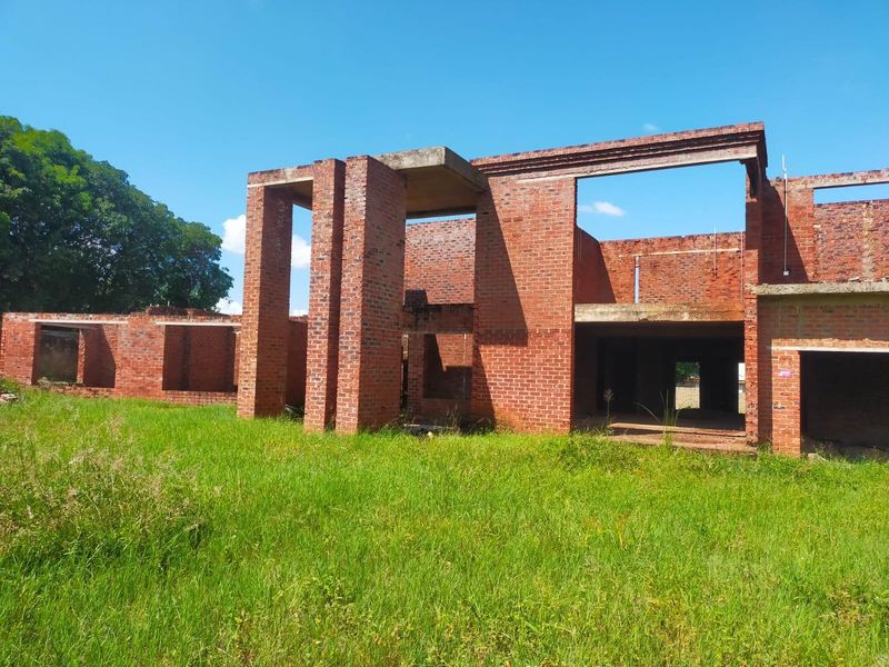 An unfinished residential structure featuring exposed brickwork and concrete framing, currently in the early stages of construction.