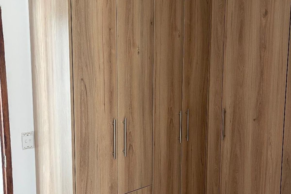 A bedroom featuring modern, floor-to-ceiling built-in wooden wardrobes with integrated drawers and sleek metal handles.