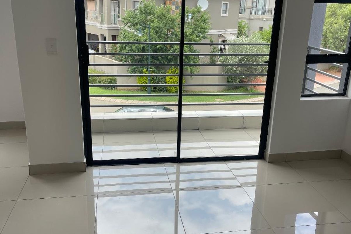 Bright living area featuring large sliding glass doors that open onto a balcony, showcasing polished tile flooring and a view of the surrounding estate.