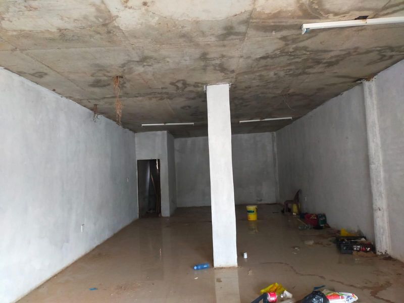 An unfinished commercial space featuring an exposed concrete ceiling, structural support column, and tiled flooring, requiring significant renovation and finishing work.