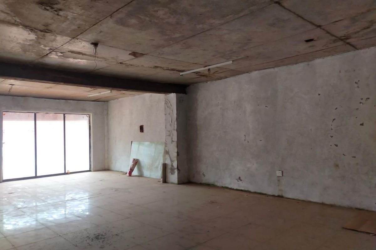 An empty, open-plan commercial space featuring tiled flooring, an exposed concrete ceiling, and large sliding glass doors, currently requiring significant renovation and cosmetic repairs.
