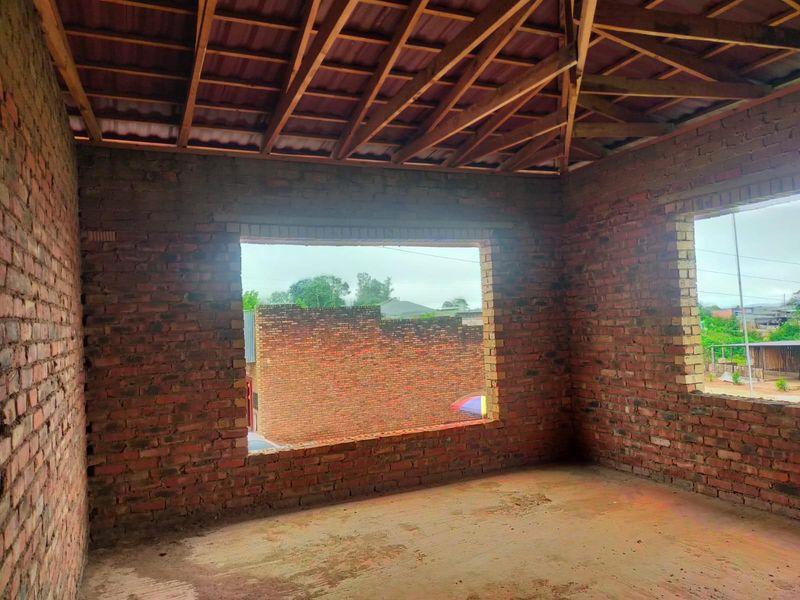 An unfinished interior space featuring exposed brick walls and timber roof trusses, currently in a shell construction state awaiting further development and finishing.