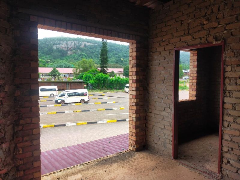 An unfinished interior space featuring exposed brick walls and open door and window frames, overlooking a commercial parking area.