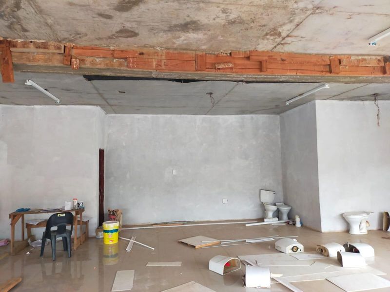 An unfinished commercial bathroom space featuring exposed concrete ceilings, tiled floors, and multiple toilet fixtures currently undergoing renovation.