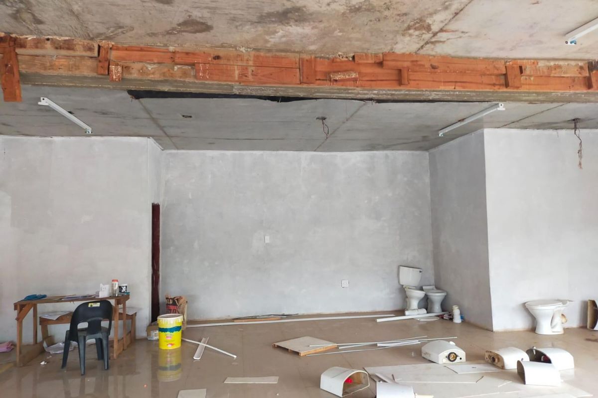 An unfinished commercial bathroom space featuring exposed concrete ceilings, tiled floors, and multiple toilet fixtures currently undergoing renovation.