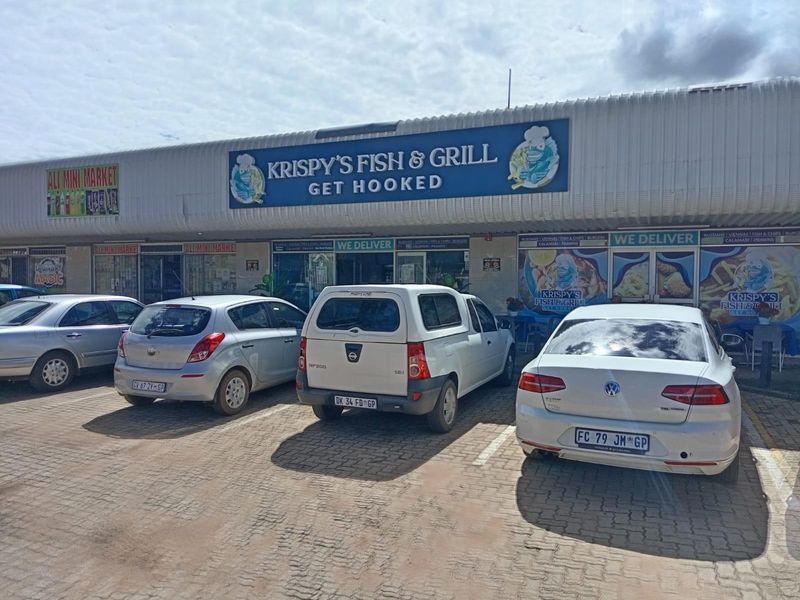 Front exterior view of a commercial restaurant building featuring a corrugated metal facade, prominent signage, and a paved parking area.