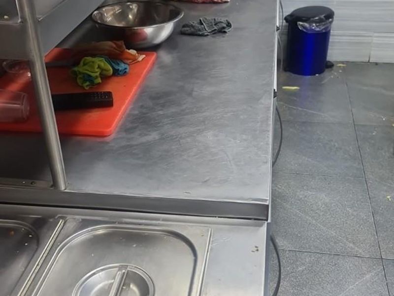 A functional commercial kitchen area featuring stainless steel prep counters, tiled flooring, and wall-mounted shelving for efficient food preparation.