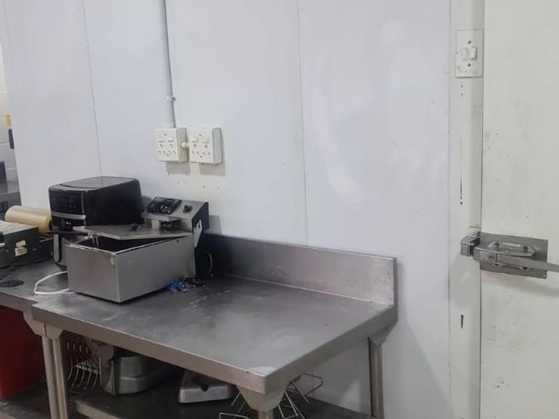 Commercial kitchen area featuring a stainless steel prep table, tiled flooring, and a walk-in cold room with integrated temperature gauges.