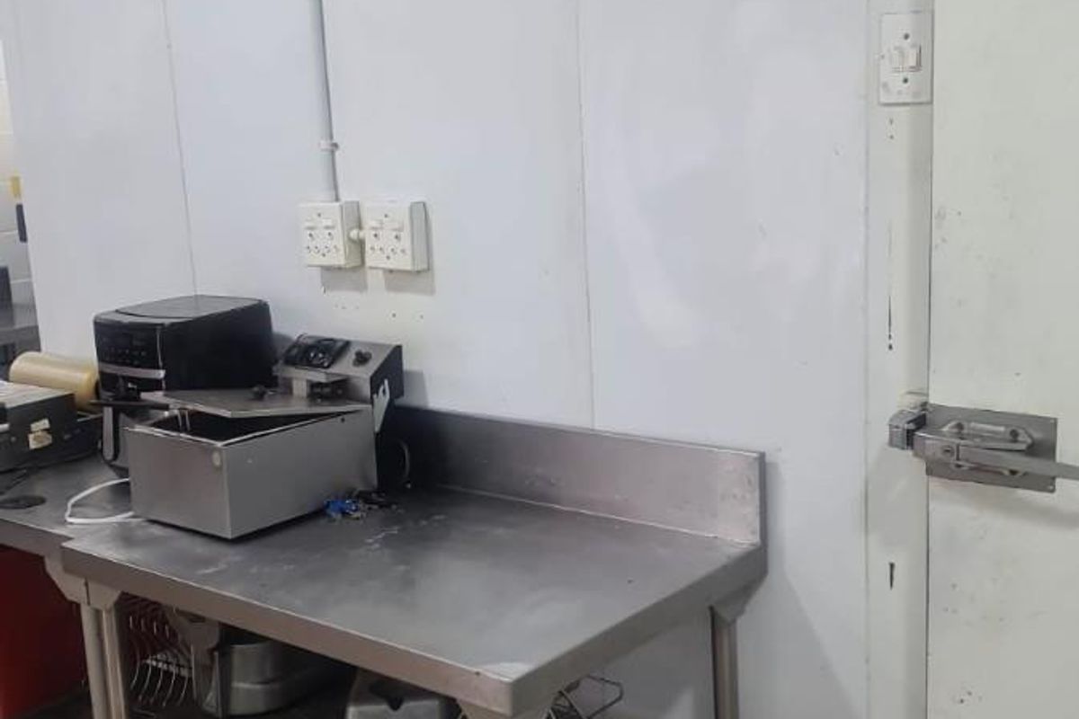 Commercial kitchen area featuring a stainless steel prep table, tiled flooring, and a walk-in cold room with integrated temperature gauges.