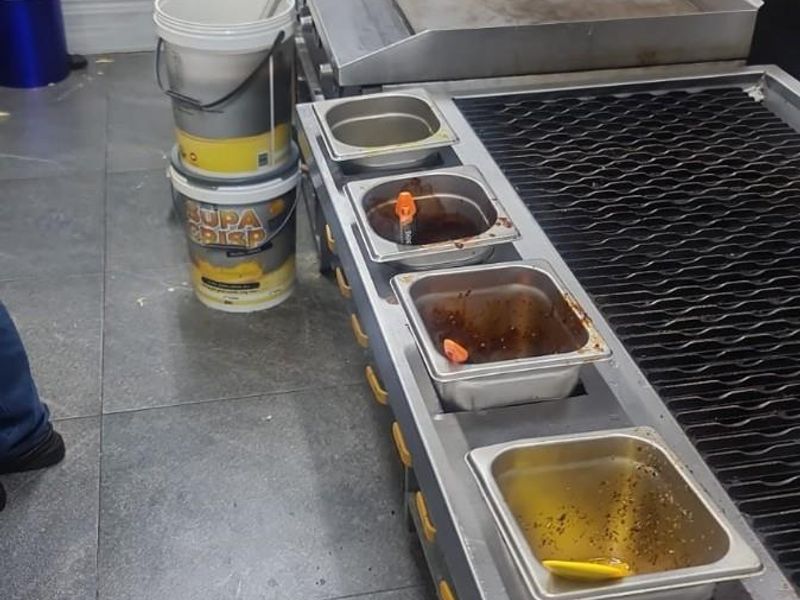 Commercial kitchen cooking station featuring a flat top grill, charbroiler, and stainless steel backsplash with tiled flooring.