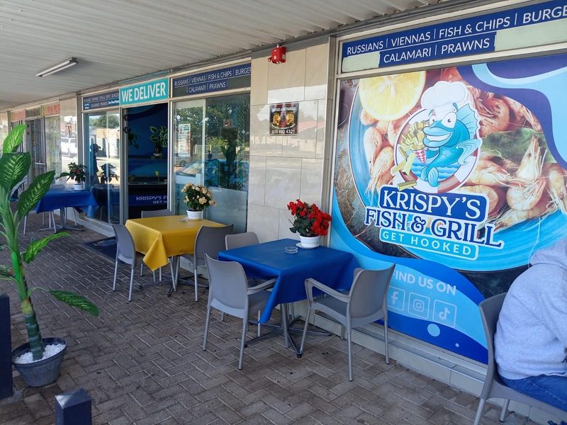 Outdoor covered seating area in front of a restaurant storefront with paved flooring and large glass display windows.