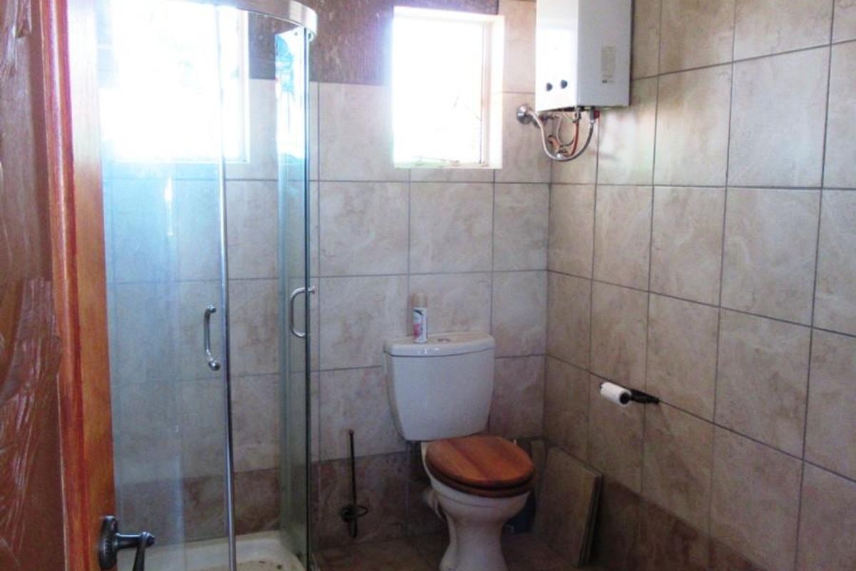 A functional bathroom featuring a corner glass shower enclosure, toilet, and wall-mounted gas water heater with full-height ceramic wall tiling.
