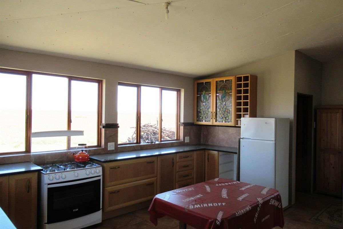 A functional kitchen featuring wooden cabinetry, granite countertops, a gas stove, and stained glass cabinet inserts with views of the surrounding farm landscape.