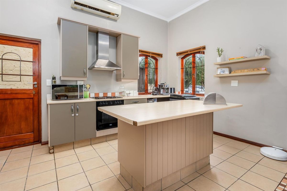 A functional kitchen featuring neutral cabinetry, a central island, stainless steel extractor fan, and tiled flooring with direct access to the exterior.