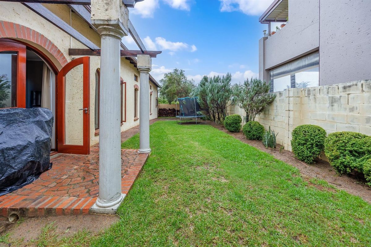 A rear garden featuring a paved patio area with decorative columns, a lawn, and a boundary wall.