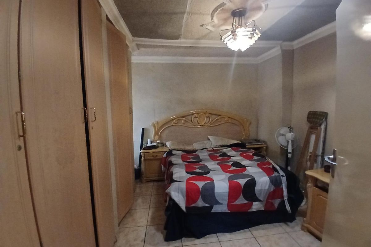 A bedroom featuring built-in cupboards, tiled flooring, and decorative ceiling detailing. The room requires cosmetic updates to improve its overall condition.