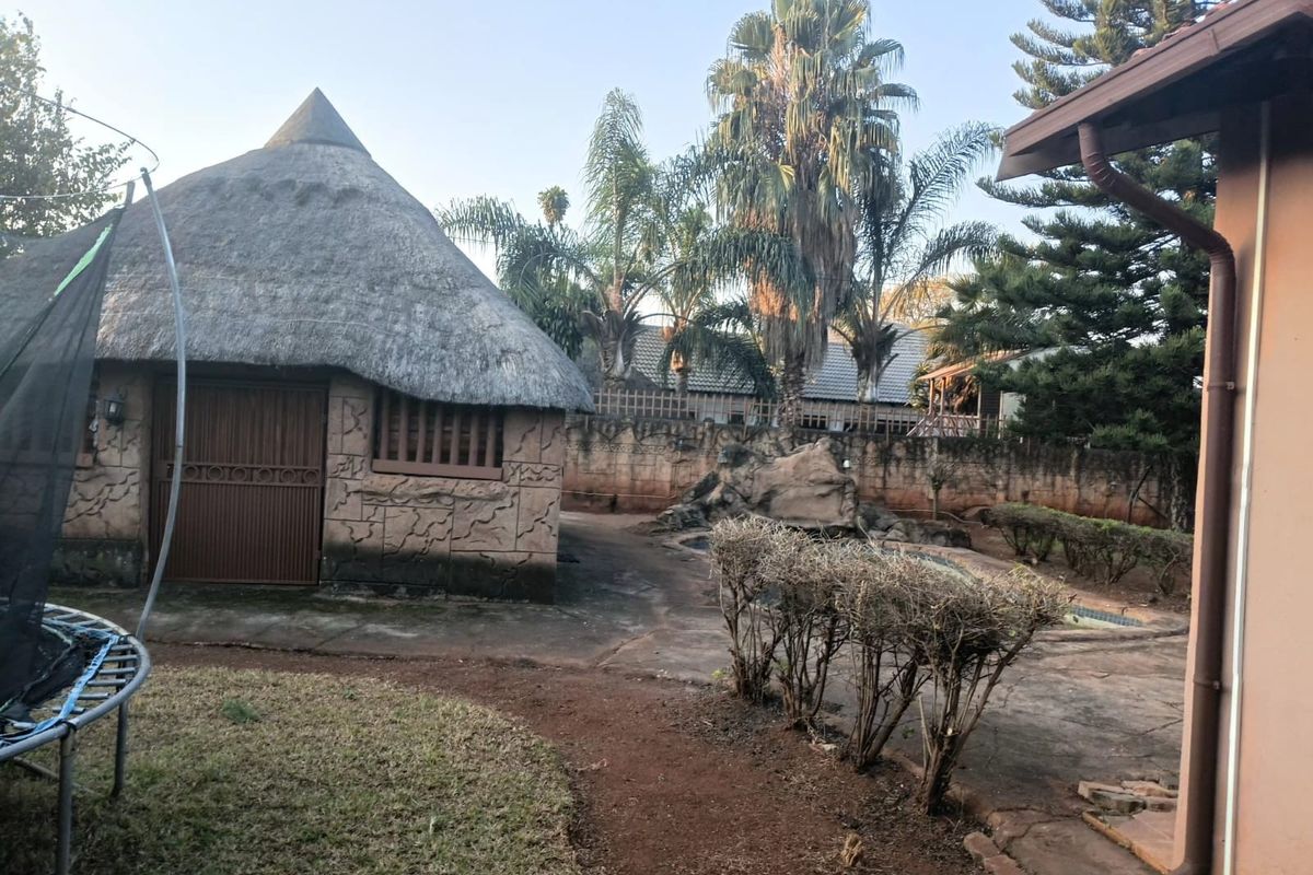 Rear garden area featuring a thatch roof lapa, swimming pool with rock feature, and paved outdoor space.