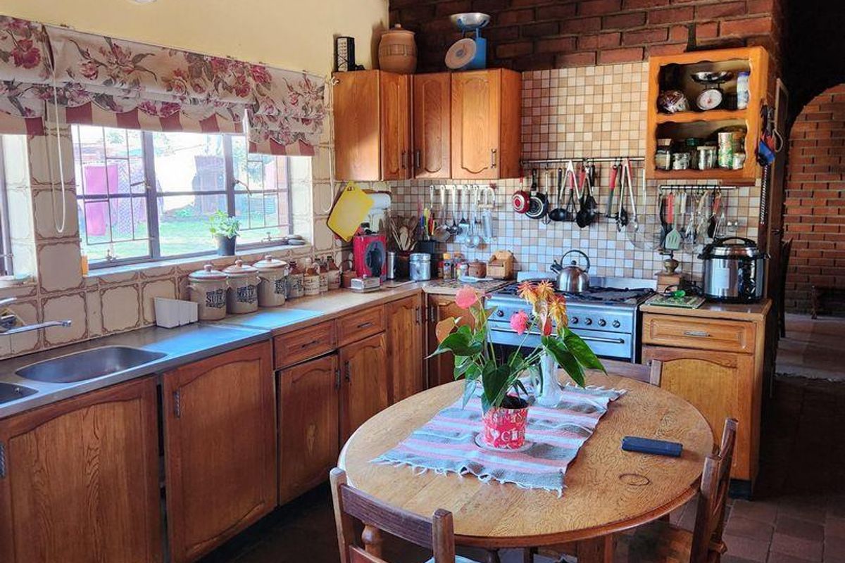 A rustic farm-style kitchen featuring wooden cabinetry, a brick feature wall, tiled flooring, and a timber-paneled ceiling with integrated stove and sink.