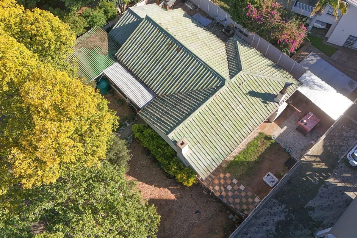 Aerial view of the property showing the metal roof structure, rear garden area, paved patio, and surrounding landscaping.