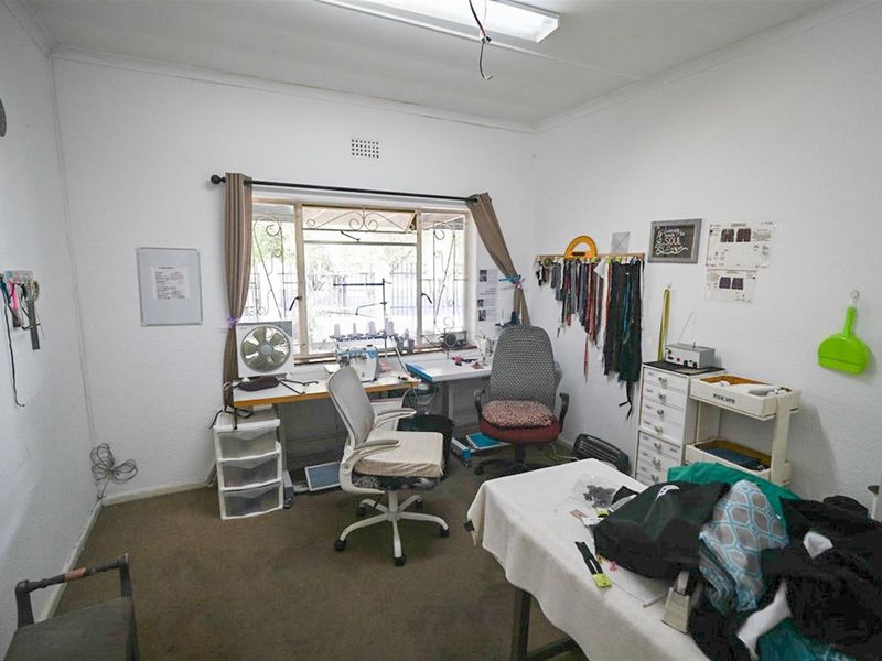 A functional office or utility room featuring a large window with security bars, carpeted flooring, and overhead lighting.