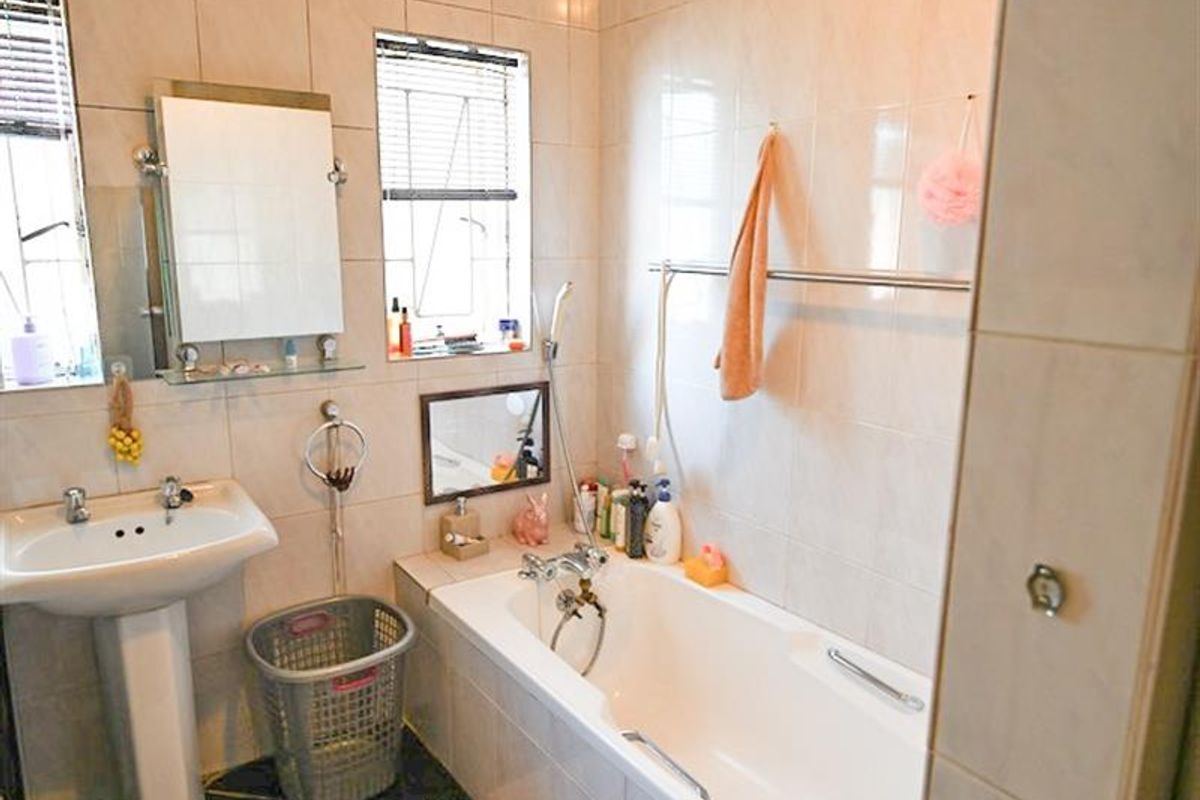 A functional bathroom featuring a pedestal basin, a built-in bathtub with shower mixer, and full-height wall tiling.