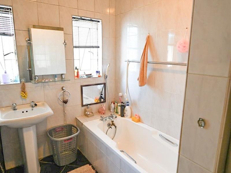 A functional bathroom featuring a pedestal basin, a built-in bathtub with shower mixer, and full-height wall tiling.