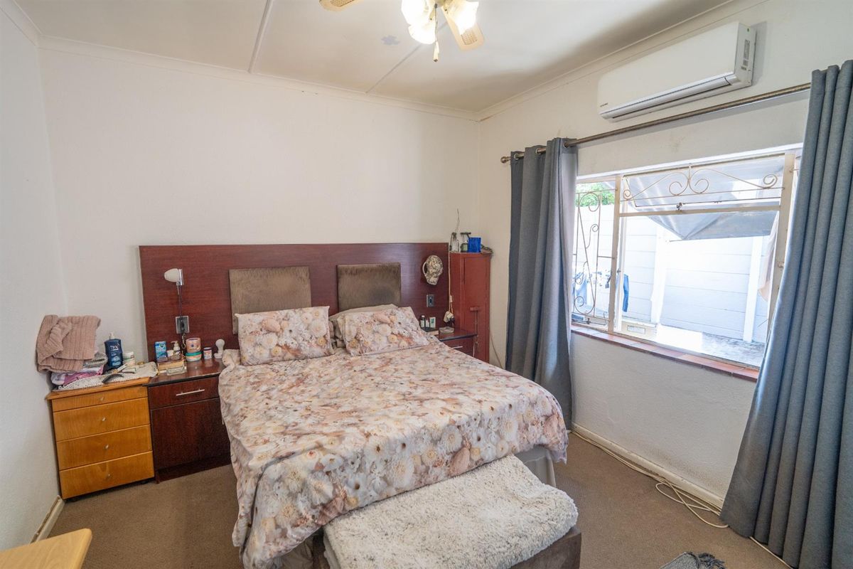 A bedroom featuring a built-in headboard, wall-mounted air conditioning unit, and security bars on the window.