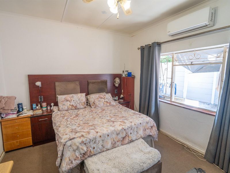 A bedroom featuring a built-in headboard, wall-mounted air conditioning unit, and security bars on the window.