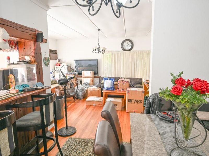 Open plan living and dining area featuring timber flooring, a breakfast bar, and traditional chandelier lighting.