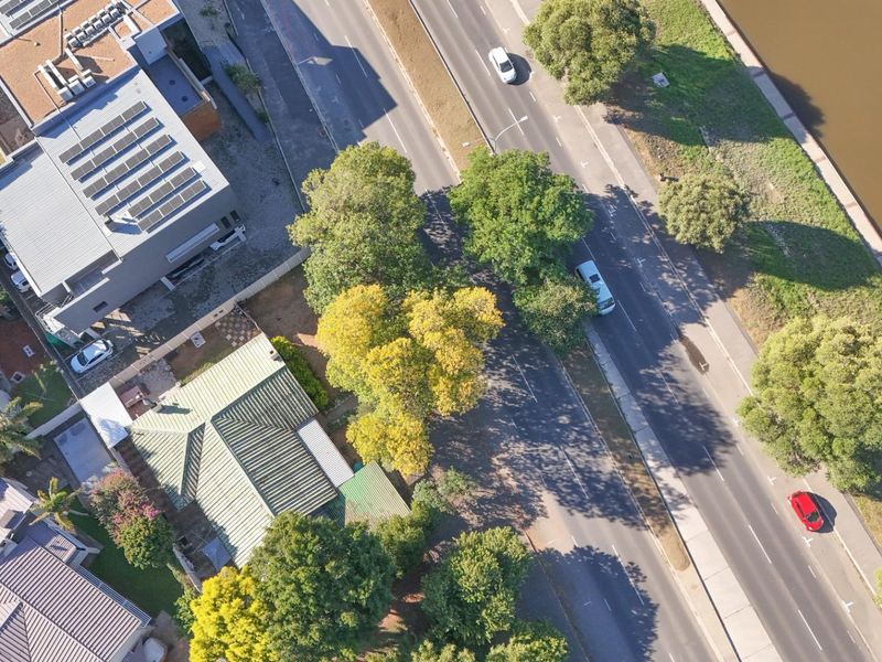 Aerial view of the property showing its location adjacent to a main road and waterway, featuring established trees and roof structure.