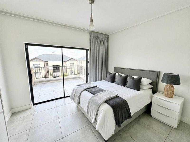 A bright bedroom featuring large sliding glass doors that open onto a private balcony, complemented by neutral tiled flooring and modern finishes.