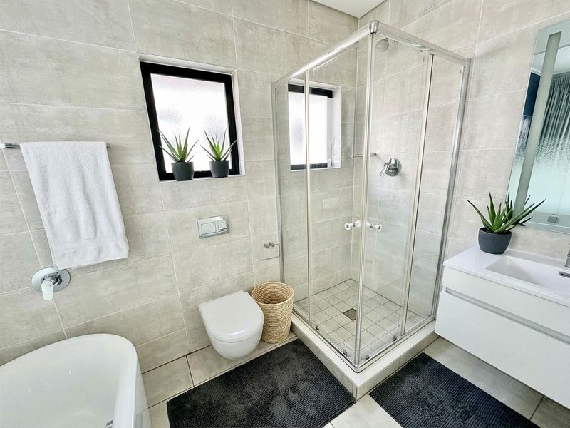 Modern bathroom featuring a glass shower enclosure, wall-mounted toilet with concealed cistern, and a sleek vanity unit with an integrated basin.