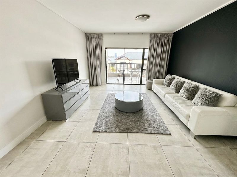 A bright and modern living room featuring large format floor tiles, a striking black accent wall, and direct access to a private balcony.
