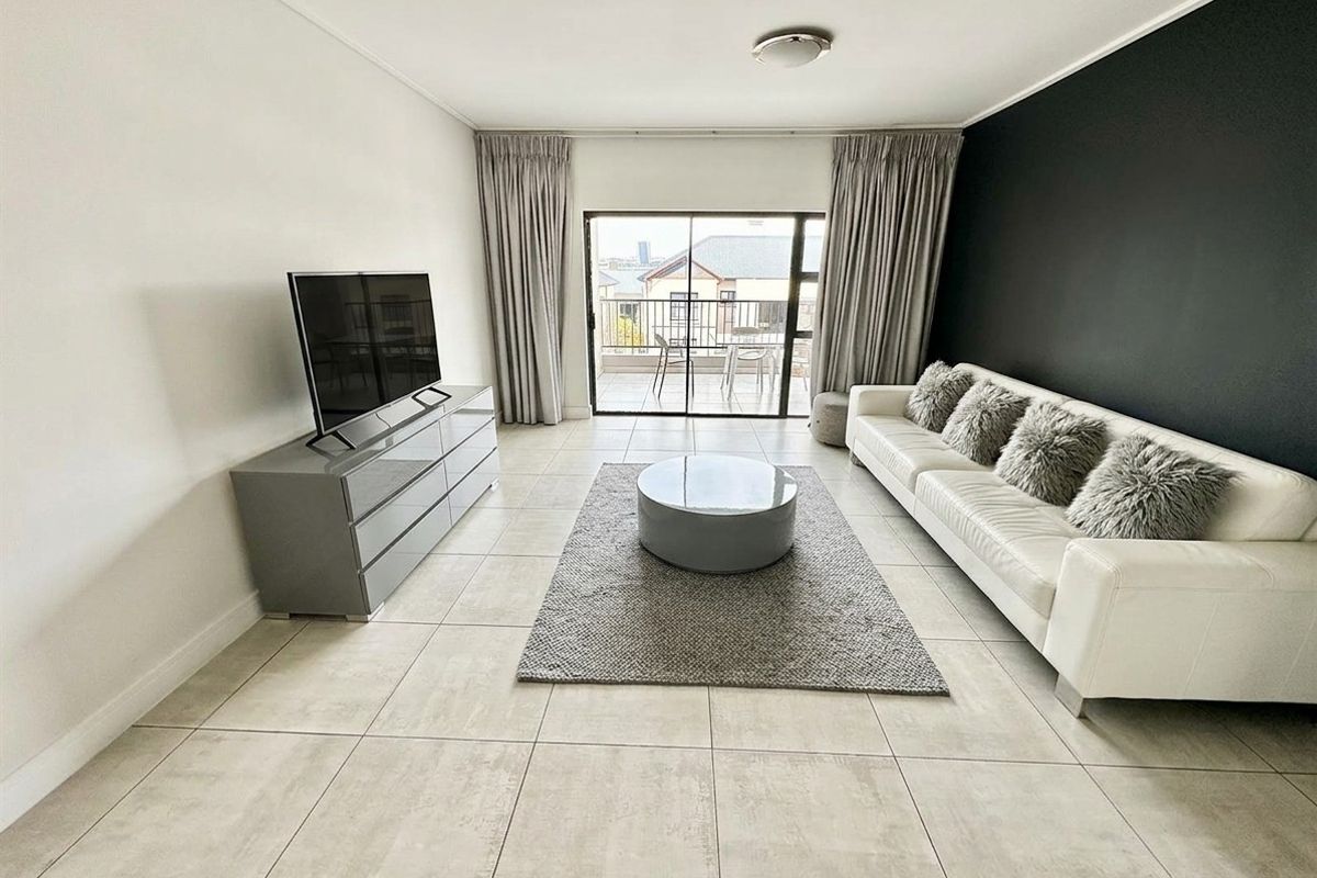 A bright and modern living room featuring large format floor tiles, a striking black accent wall, and direct access to a private balcony.