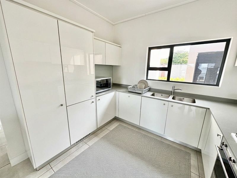 Modern kitchen featuring sleek white cabinetry, stone countertops, a double stainless steel sink, and tiled flooring with ample storage space.