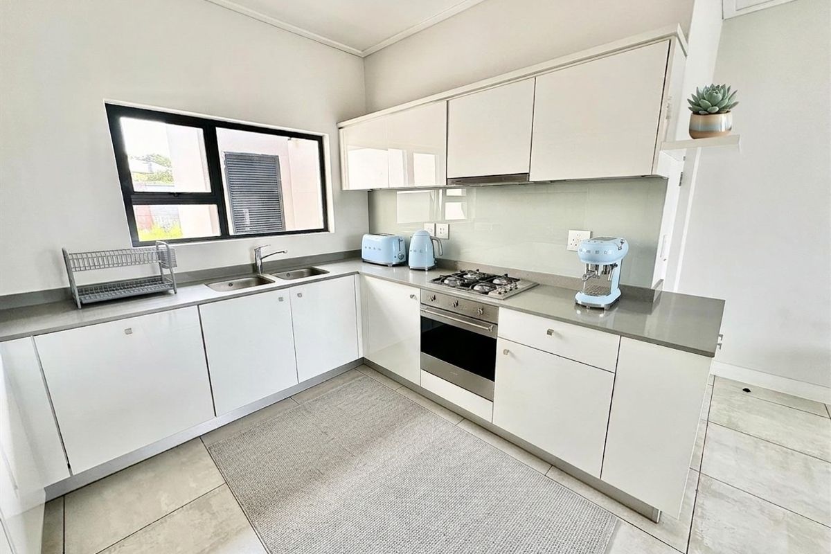 A modern, well-maintained kitchen featuring sleek white cabinetry, stone countertops, a gas hob, and integrated oven, complemented by neutral tiled flooring.