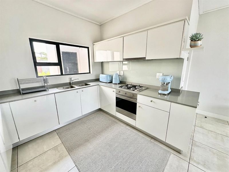 A modern, well-maintained kitchen featuring sleek white cabinetry, stone countertops, a gas hob, and integrated oven, complemented by neutral tiled flooring.