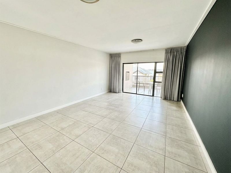 Spacious, empty living area featuring neutral tiled flooring, a dark accent wall, and sliding glass doors leading to an outdoor balcony.
