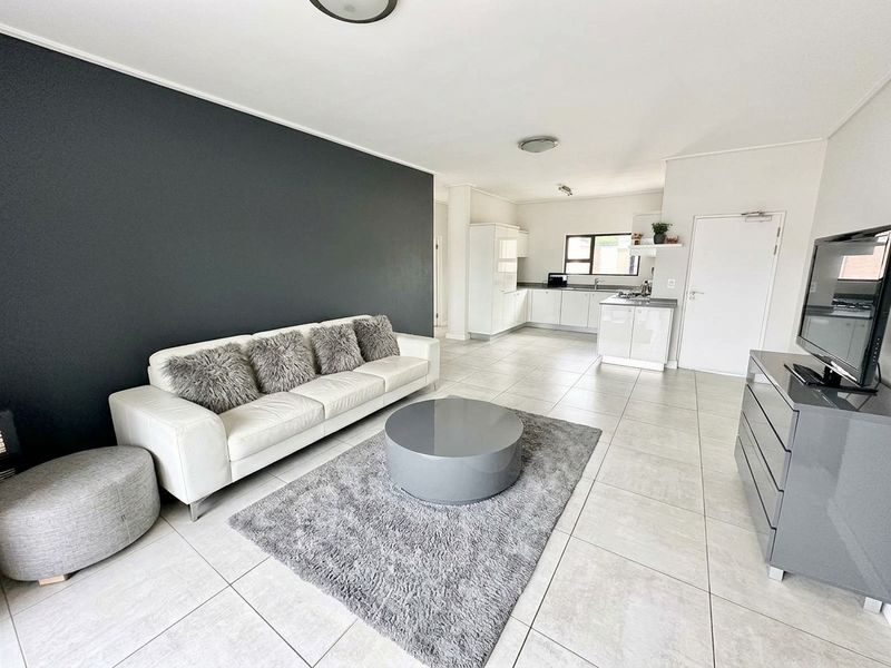 Spacious open-plan living area featuring a modern kitchen with built-in cabinetry, a central island, and a striking dark accent wall.