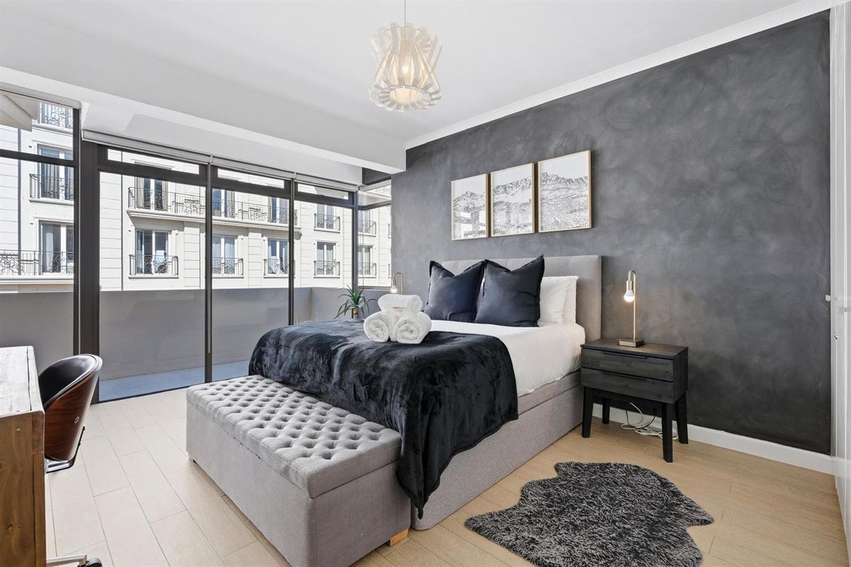 Modern bedroom featuring light wood-look flooring, a striking dark textured feature wall, and floor-to-ceiling glass sliding doors opening onto a private balcony.