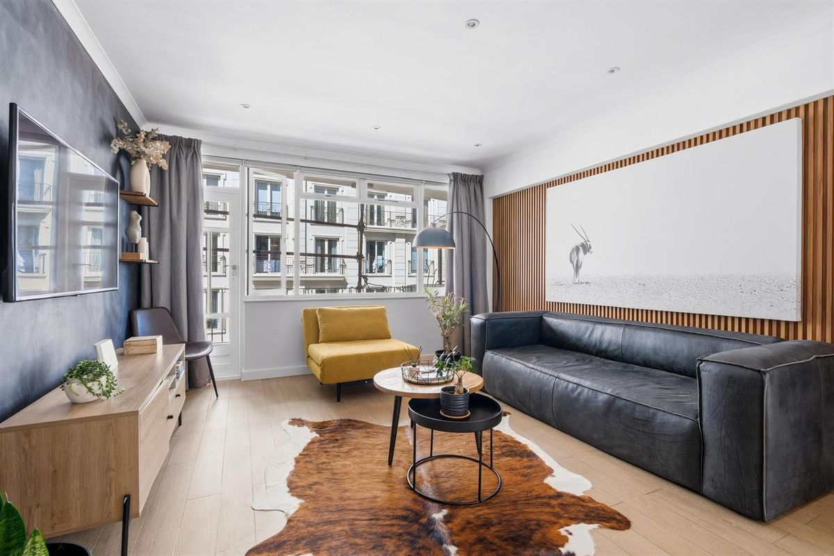 A modern living room featuring timber slat wall paneling, recessed downlighting, and large windows providing natural light and an urban outlook.