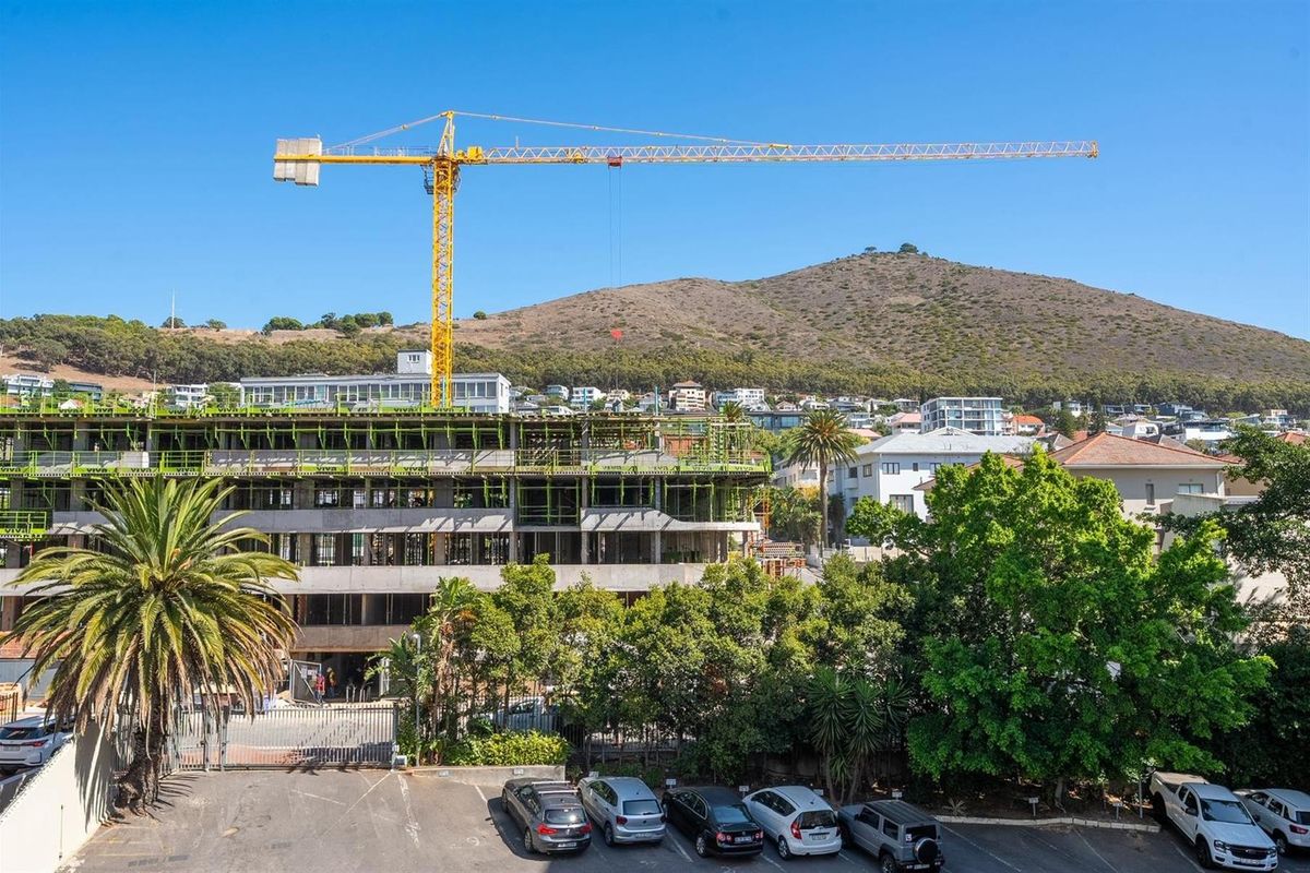 An aerial view of a multi-story apartment building currently under construction, featuring a prominent yellow tower crane and surrounding residential neighborhood.
