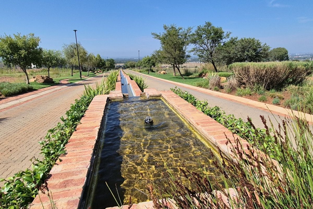 A well-maintained landscaped garden featuring a long brick water feature and paved walkways leading through the residential estate.