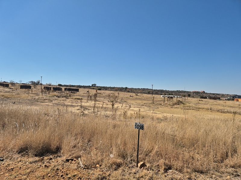 A view of a vacant residential plot featuring dry grass and a clear boundary marker, ready for development.